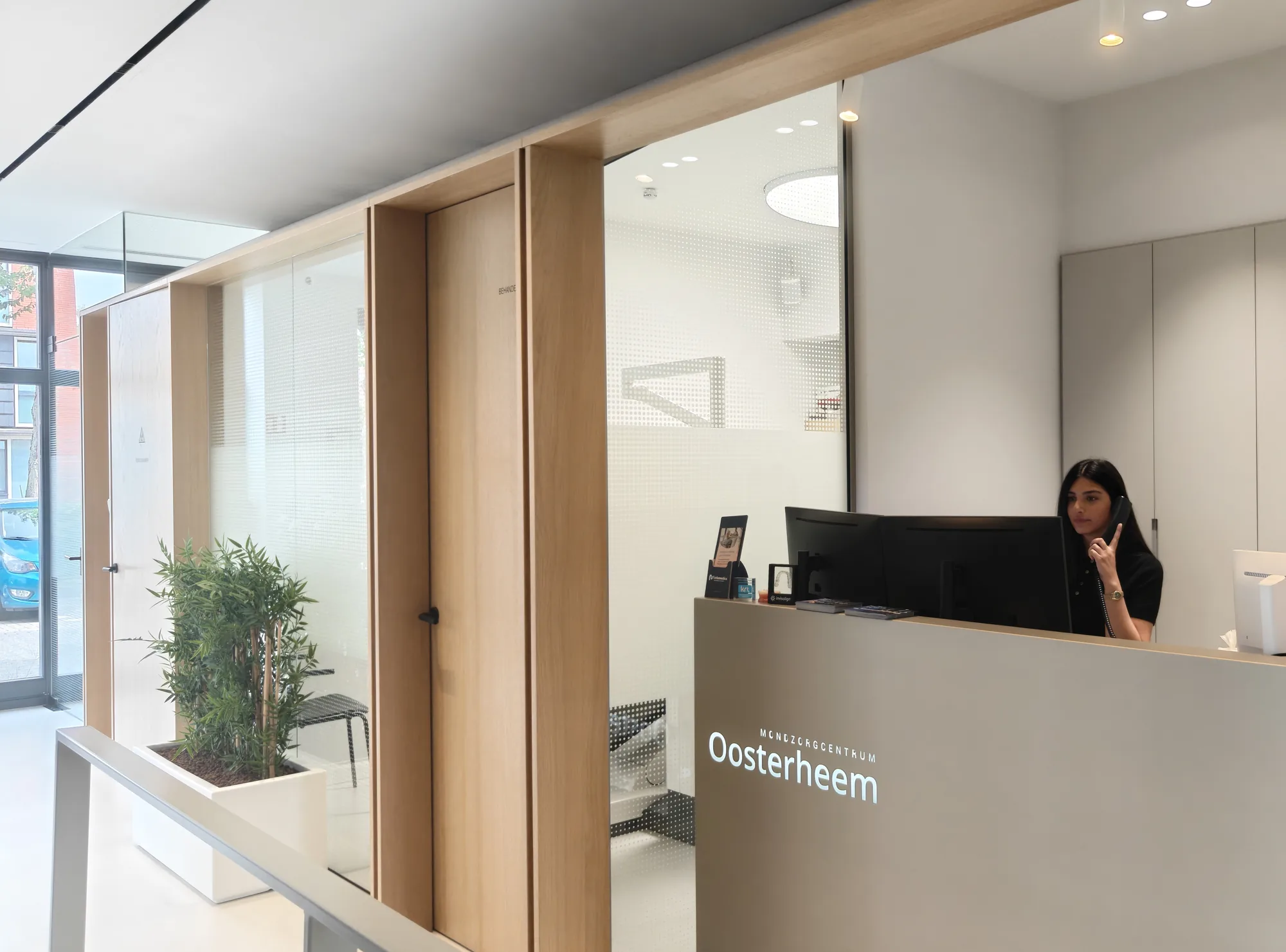 De lichte ontvangstruimte van Mondzorgcentrum Oosterheem, met een collega aan het werk achter de balie